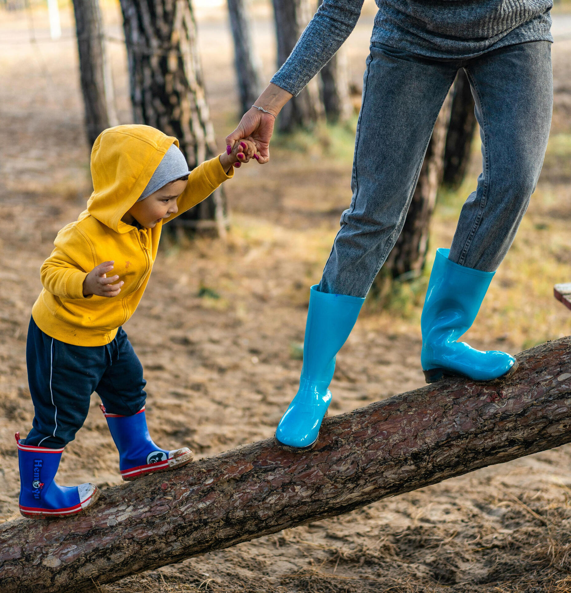 A child reluctantly walks on a log holding an adult's hand. Photo by Alex P via Pexels.